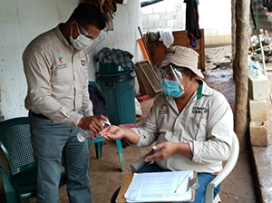 image shows two people wearing masks and one is giving hand gel to the other